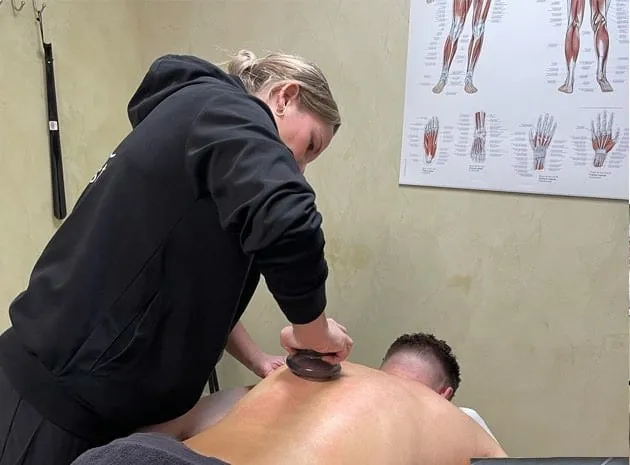 Masseuse behandelt de rug van een cliënt met een guasha-steen